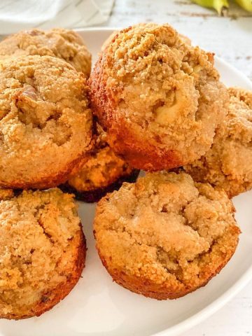 Banana bread muffins on white plate with bananas in the background.