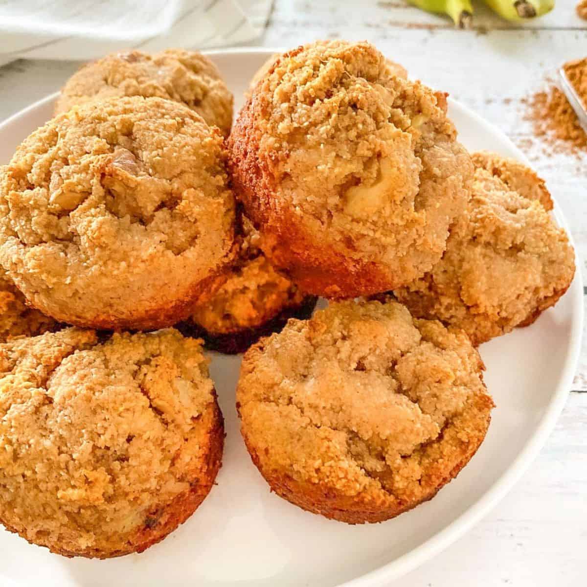 Banana bread muffins on white plate with bananas in the background.
