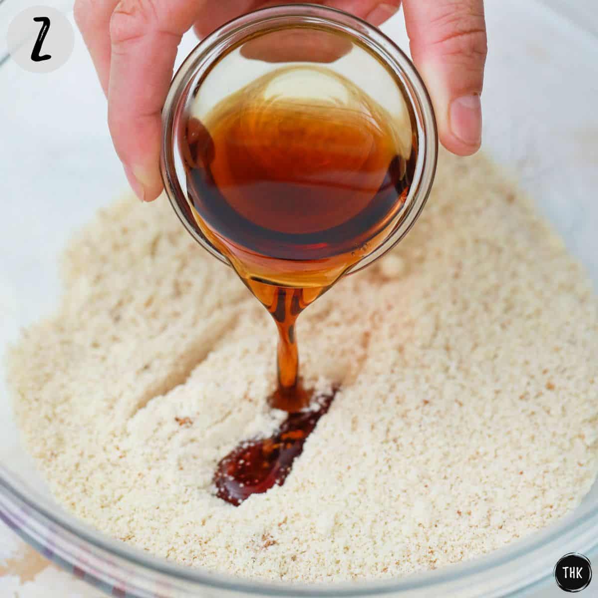 Maple syrup being poured over bowl of dry ingredients.