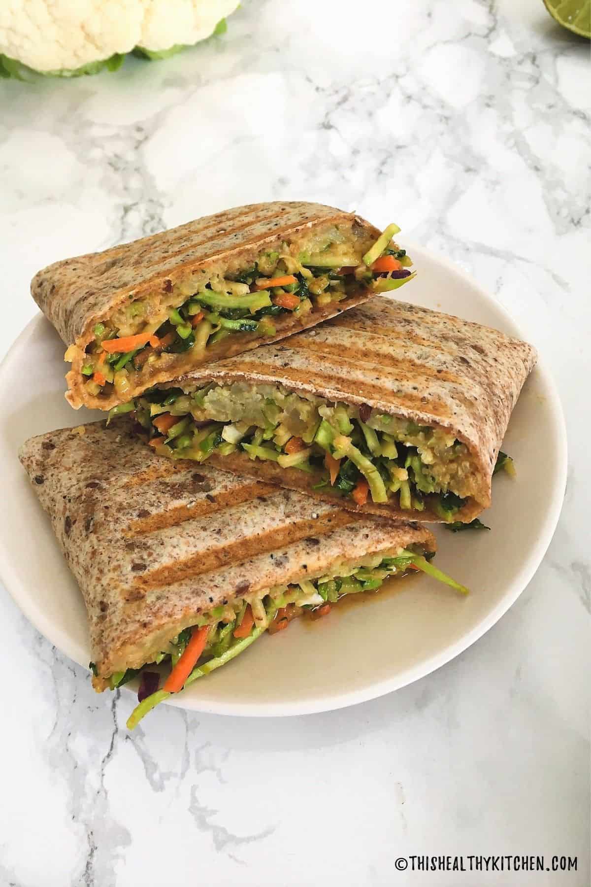 Halved veggie wraps resting on white plate.