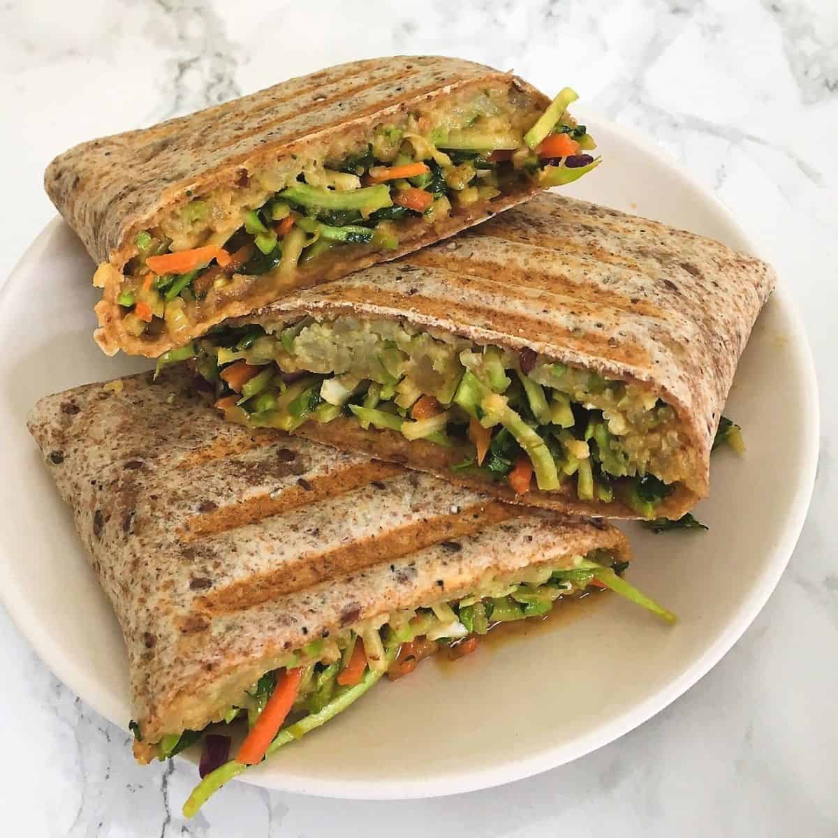 Halved veggie wraps resting on white plate.