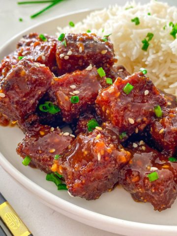 Side view of tofu with red sauce and rice on the side.
