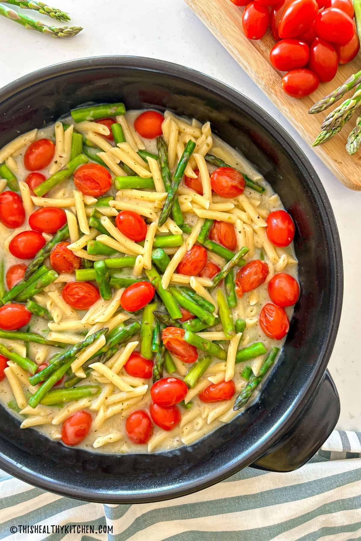 Tomato and asparagus pasta in a light creamy sauce in large black skillet.