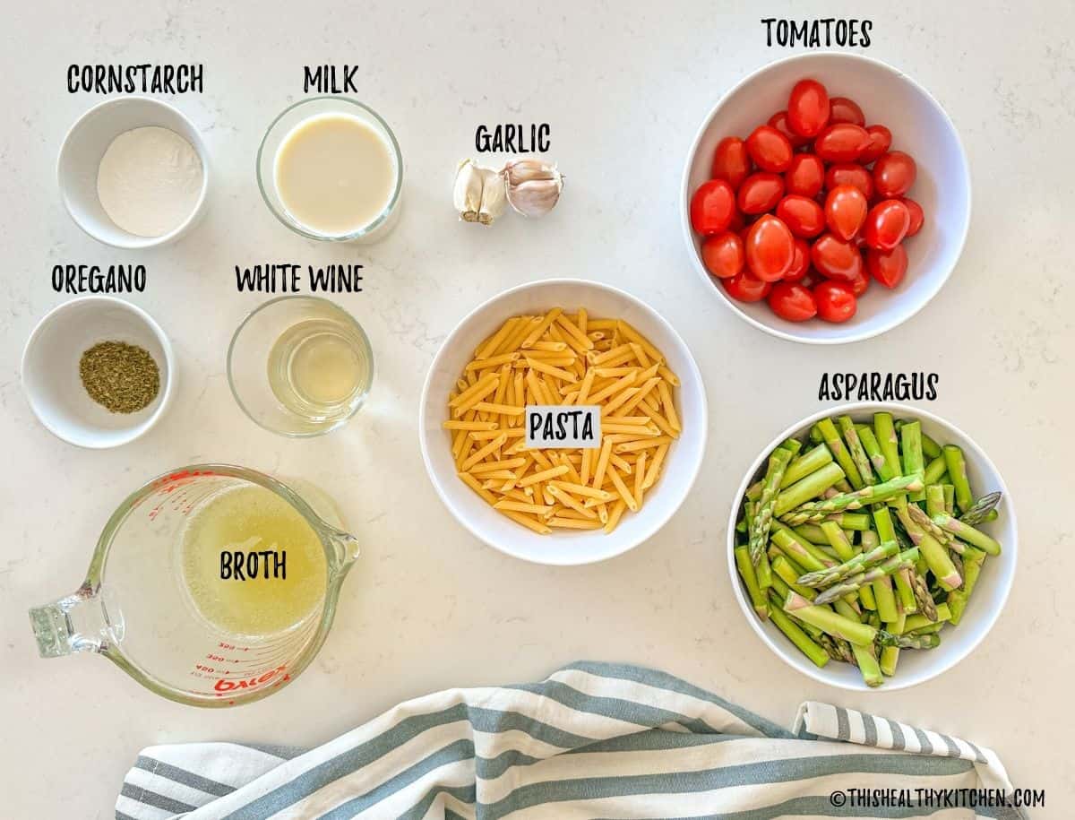 Ingredients to make asparagus tomato pasta in prep bowls on kitchen countertop.