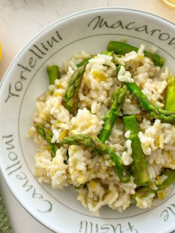 Risotto with asparagus in round bowl with lemon on the side.