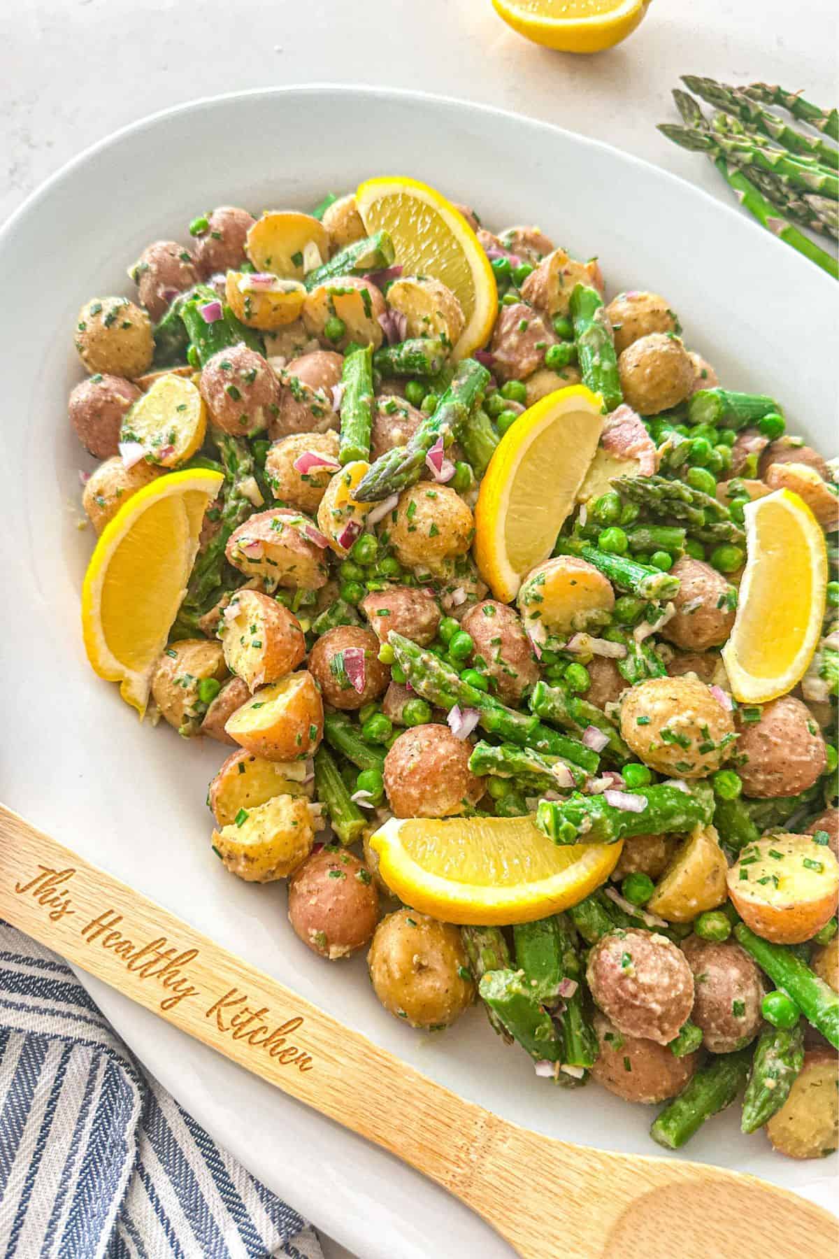 Potato asparagus salad in large white platter with lemon wedges on top.