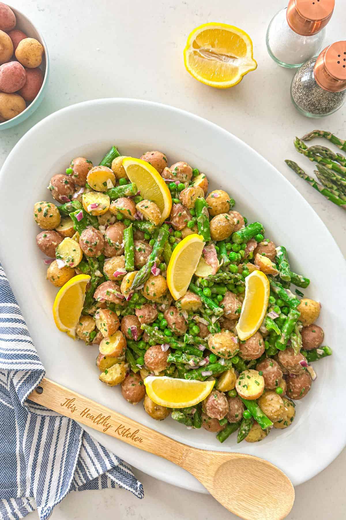 Potato asparagus salad in large white platter with lemon wedges on top and salt and pepper shaker beside it,