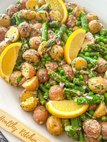 Potato asparagus salad in large white platter with lemon wedges on top.