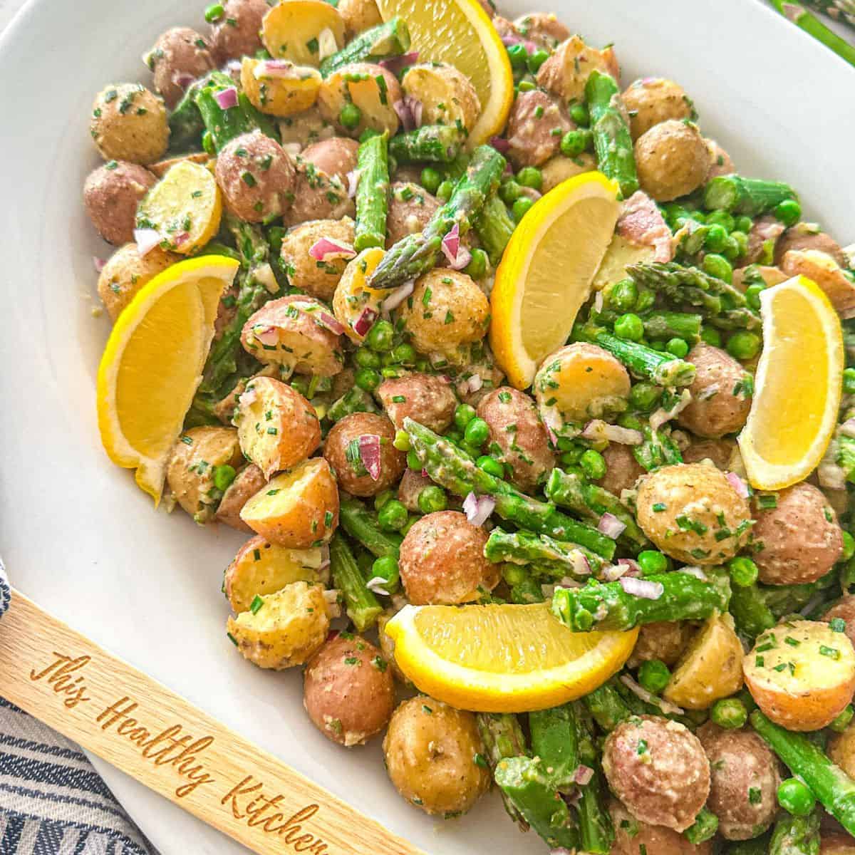 Potato asparagus salad in large white platter with lemon wedges on top.