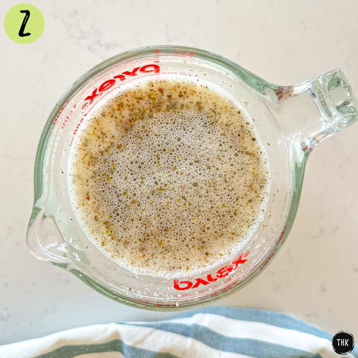 Measuring cup with white pasta sauce inside.