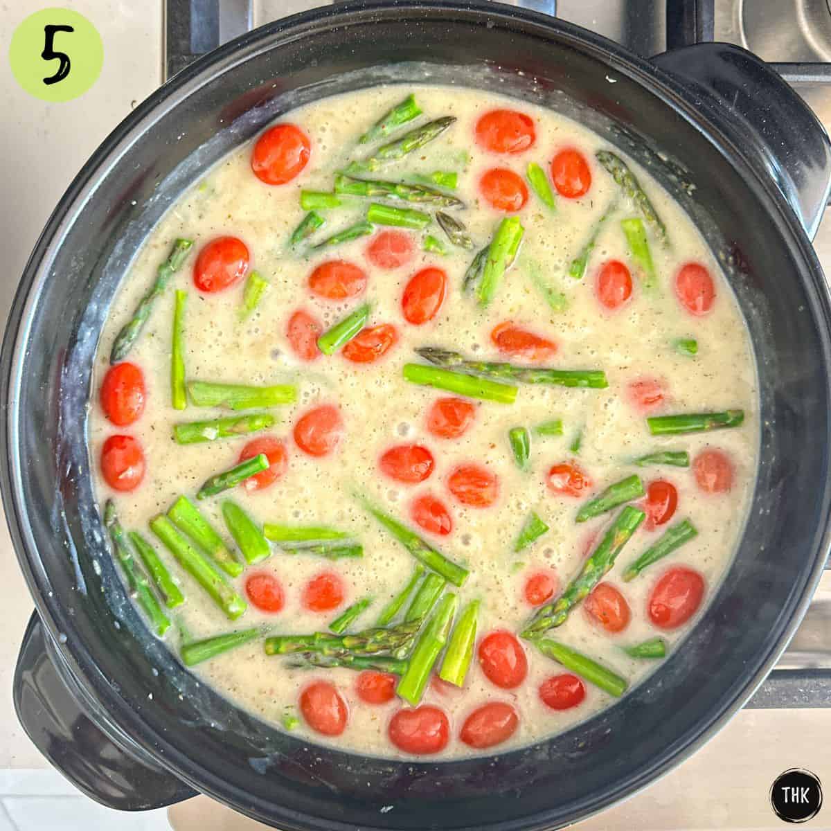 White sauce in large skillet with cherry tomatoes and asparagus inside.