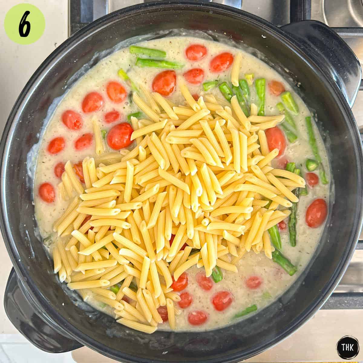 White pasta sauce in large skillet with asparagus, tomato and penne pasta.