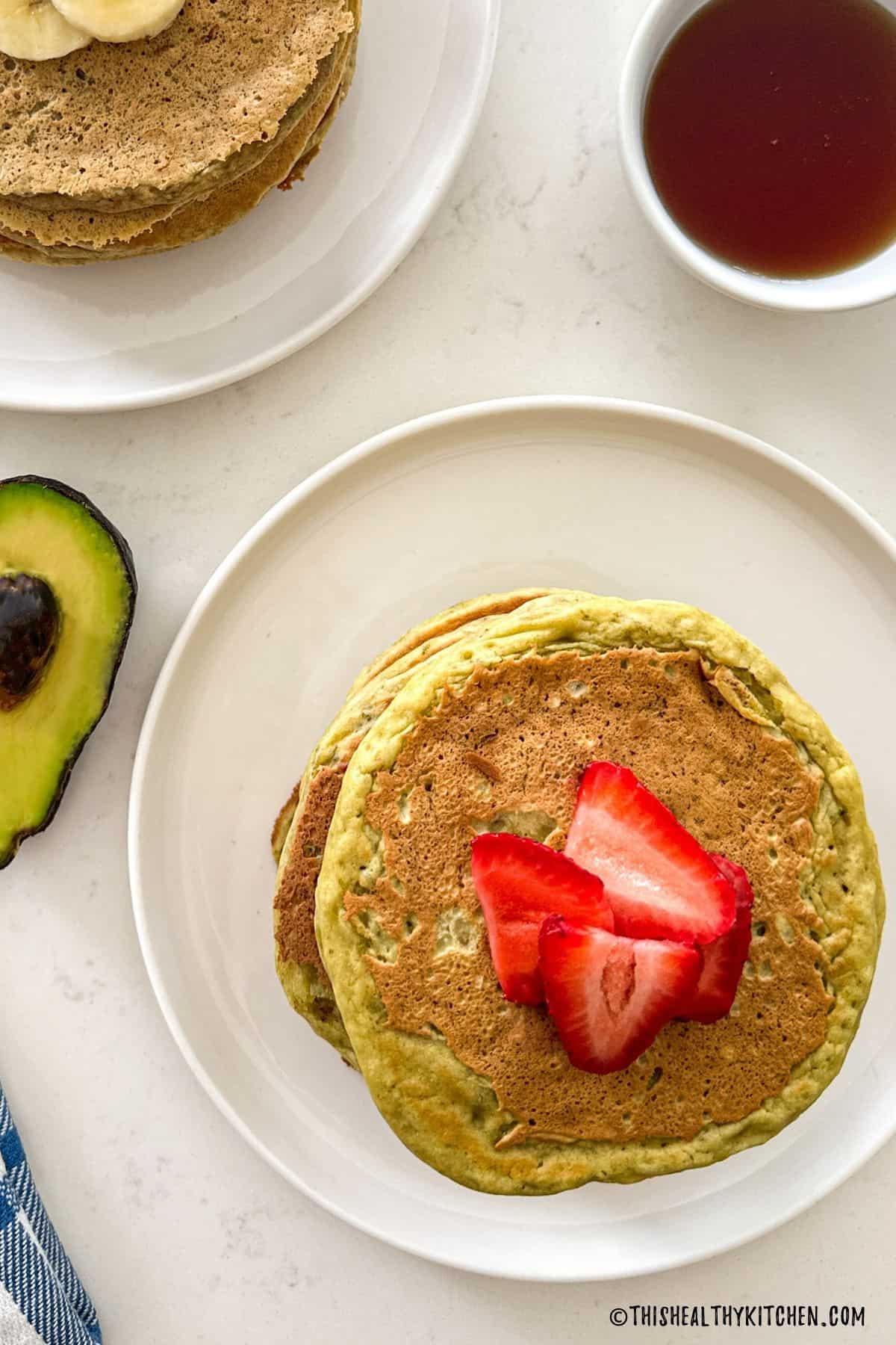Birds eye view of two plates with pancakes on top and sliced strawberries on top.
