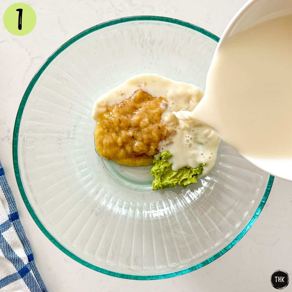 Large glass bowl with mashed banana and avocado and milk being poured on top.