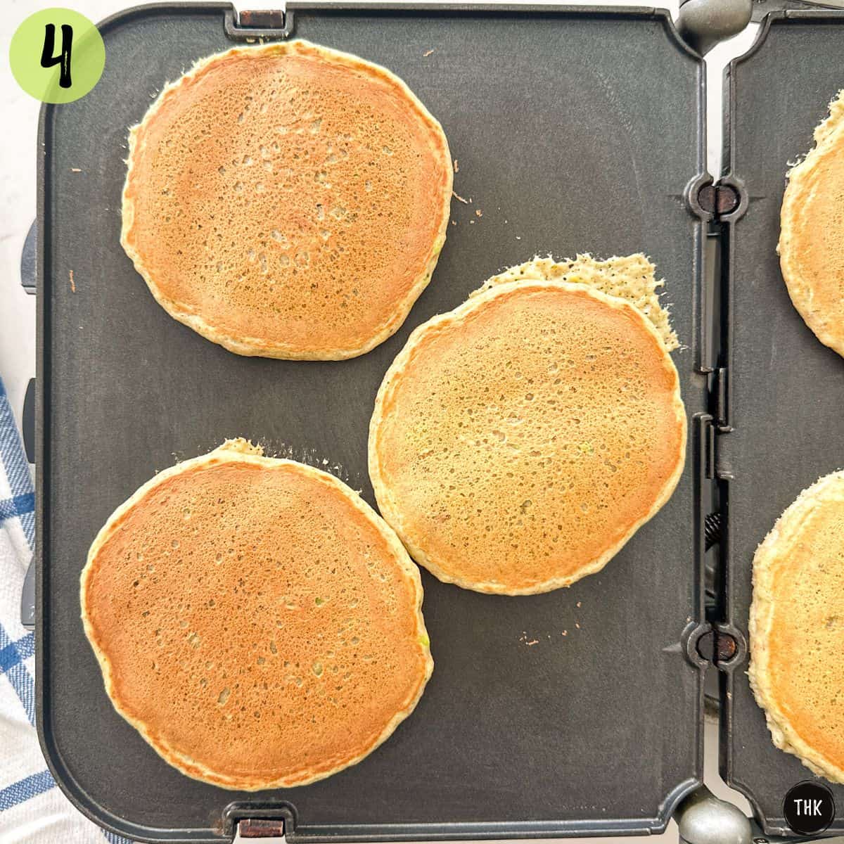 Pancakes cooking on griddle that have been flipped.