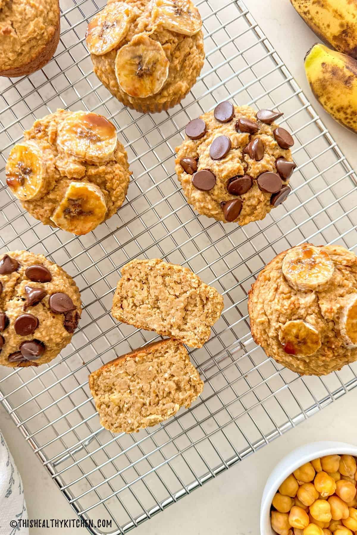 Banana muffins on wire rack with one of them sliced in half to show the inside.