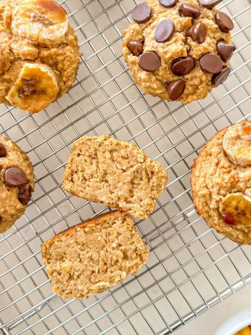 Banana muffins on wire rack with one of them sliced in half to show the inside.