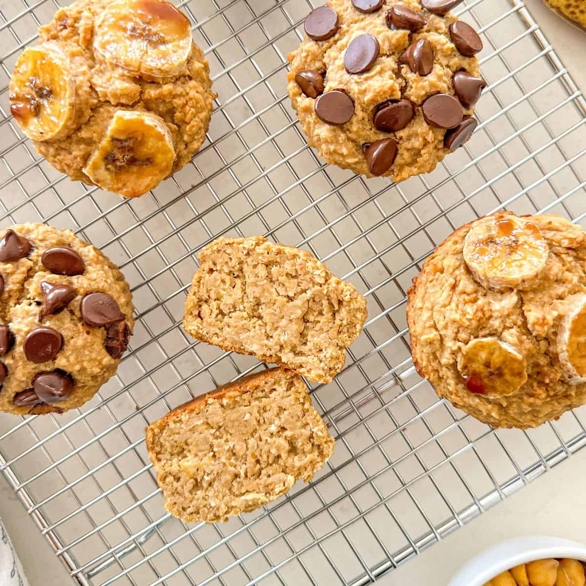 Banana muffins on wire rack with one of them sliced in half to show the inside.