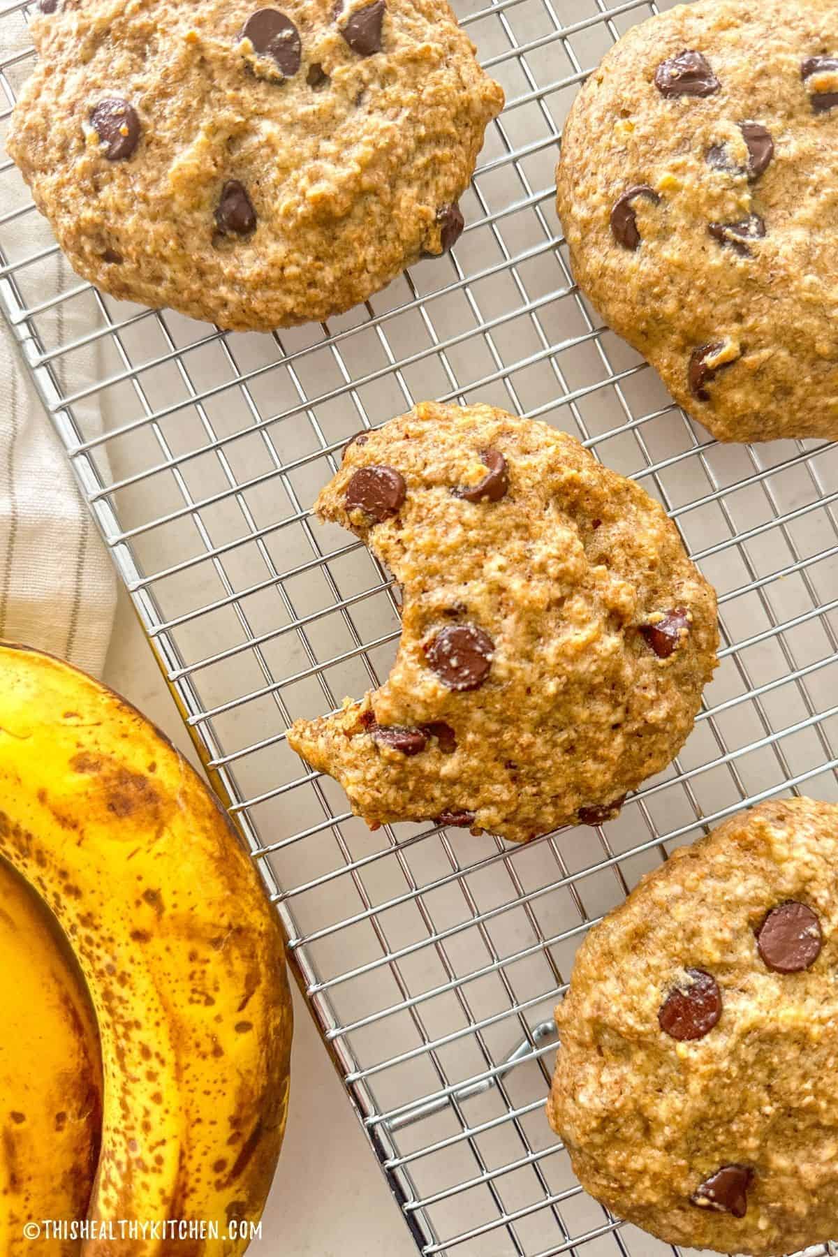 Banana chocolate chip cookies on wire rack with bite taken out of one cookie.