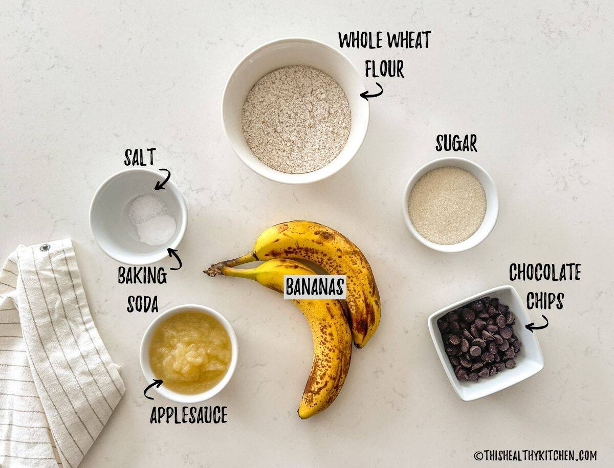 Bananas, flour, sugar, chocolate chips, applesauce, baking soda and salt in prep bowls on countertop.