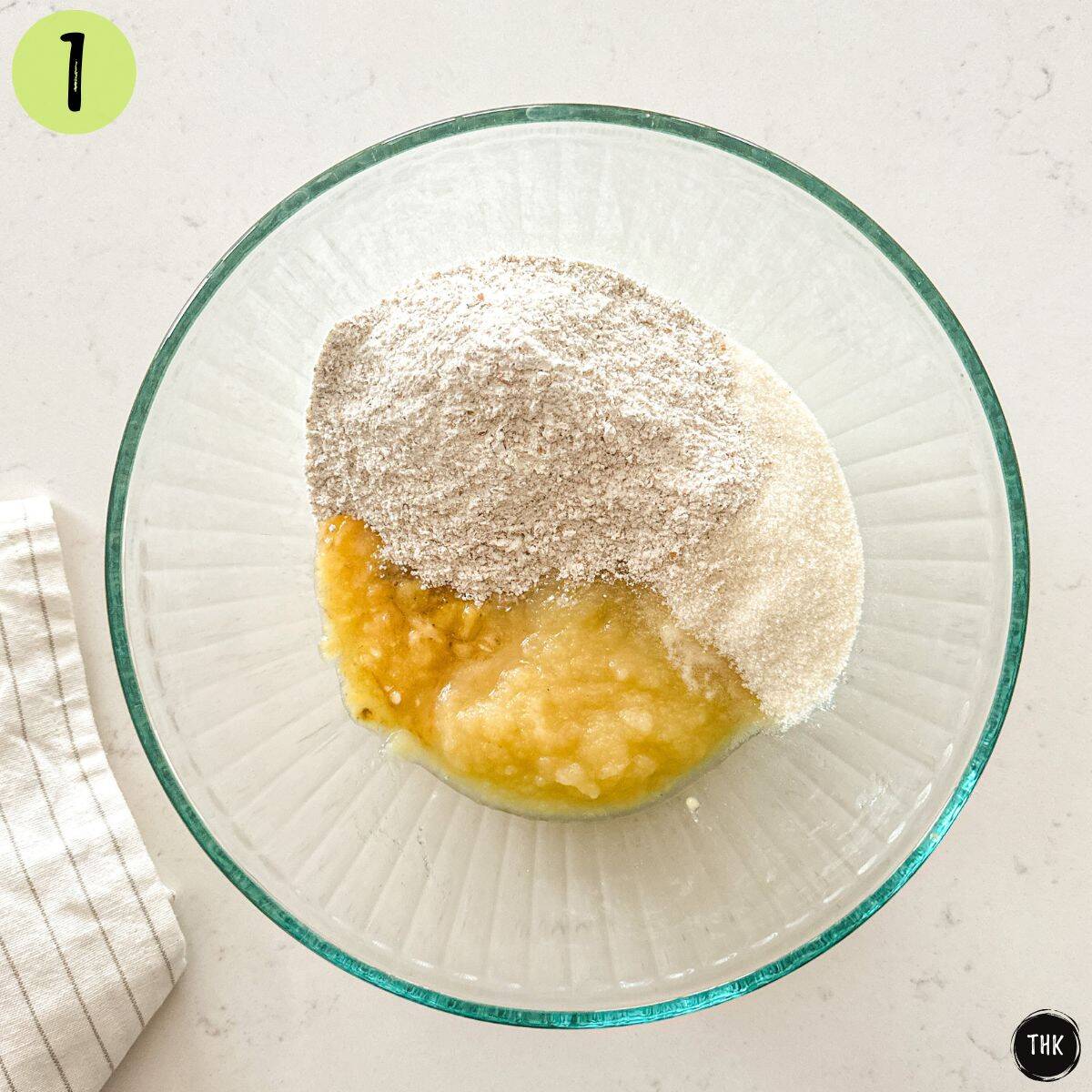 Large glass bowl with mashed bananas, applesauce and flour inside.