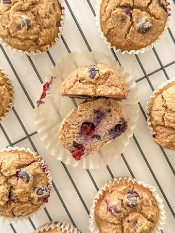 Muffin sliced in half on wire rack with more muffins all around it.