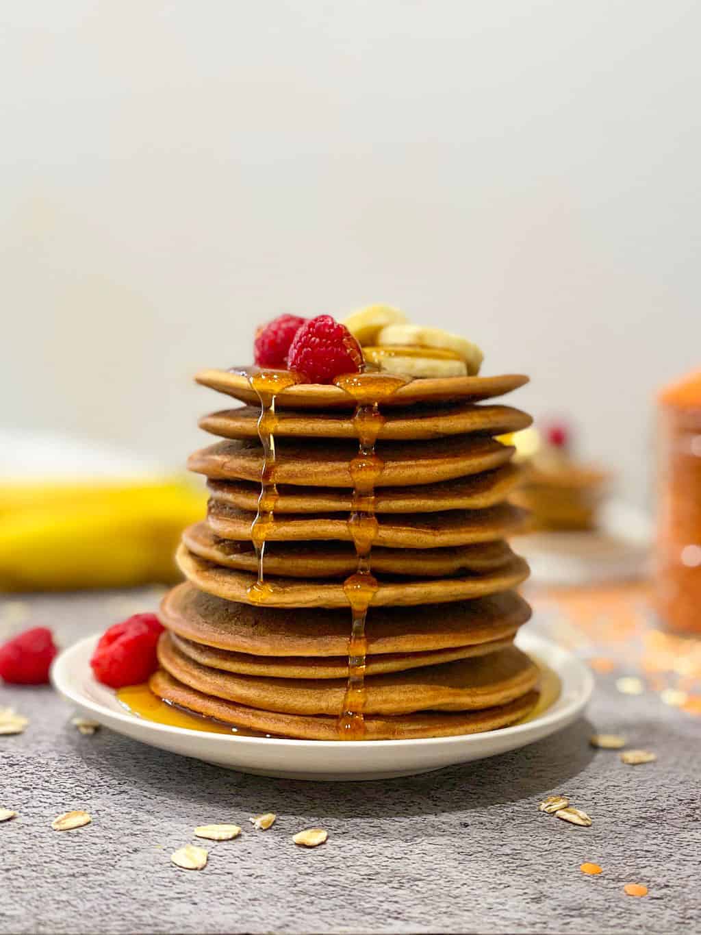 lentil pancakes stacked on plate with fruit on top and syrup dripping down.
