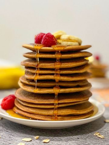 lentil pancakes stacked on plate with fruit on top and syrup dripping down.
