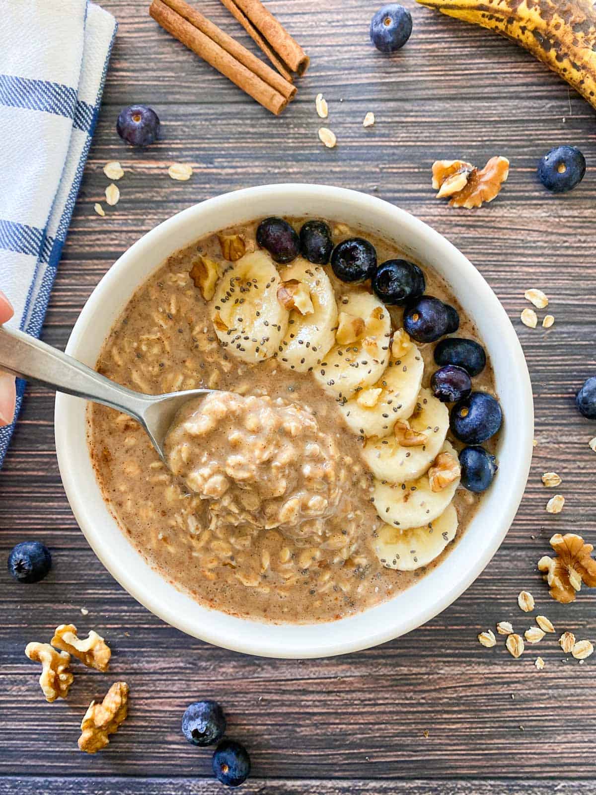 Spoonful of oatmeal being held above bowl of banana overnight oats.