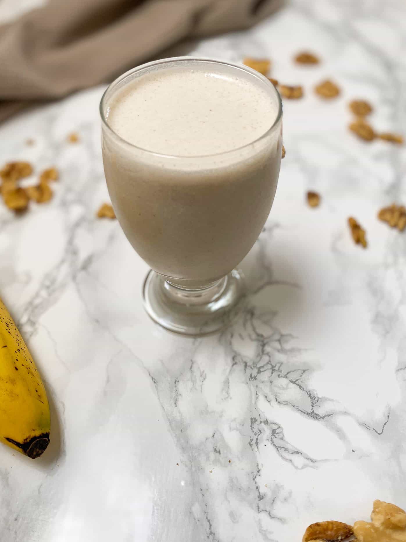 banana walnut smoothie in glass cup with walnuts and banana scattered around