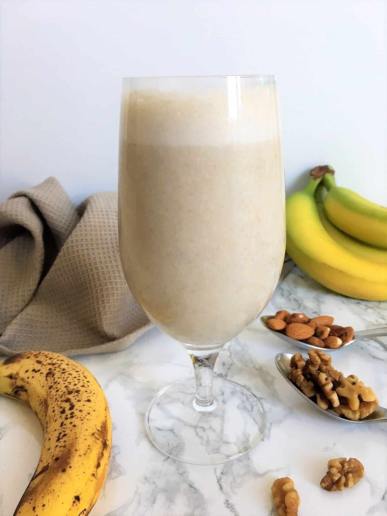 glass filled with banana smoothie with nuts and bananas on counter beside glass
