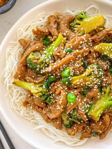 White bowl with rice noodles and soy curls and broccoli on top.