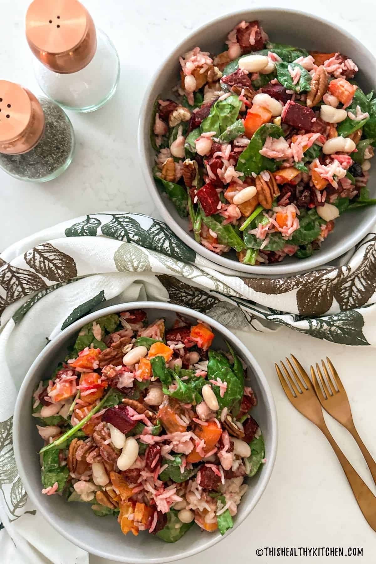 Two bowls of beet and sweet potato salad with salt and pepper shakers on the side.
