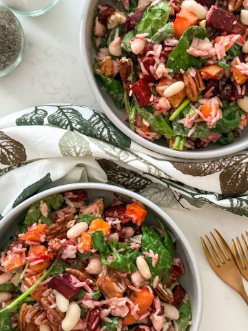 Two bowls of beet and sweet potato salad with salt and pepper shakers and forks on the side.