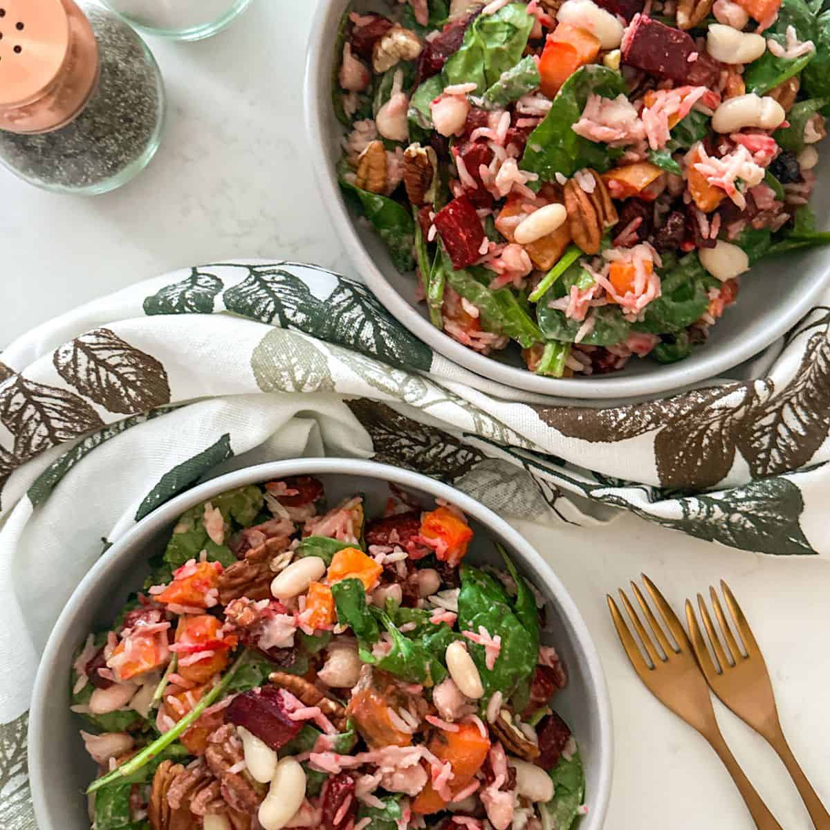 Two bowls of beet and sweet potato salad with salt and pepper shakers and forks on the side.