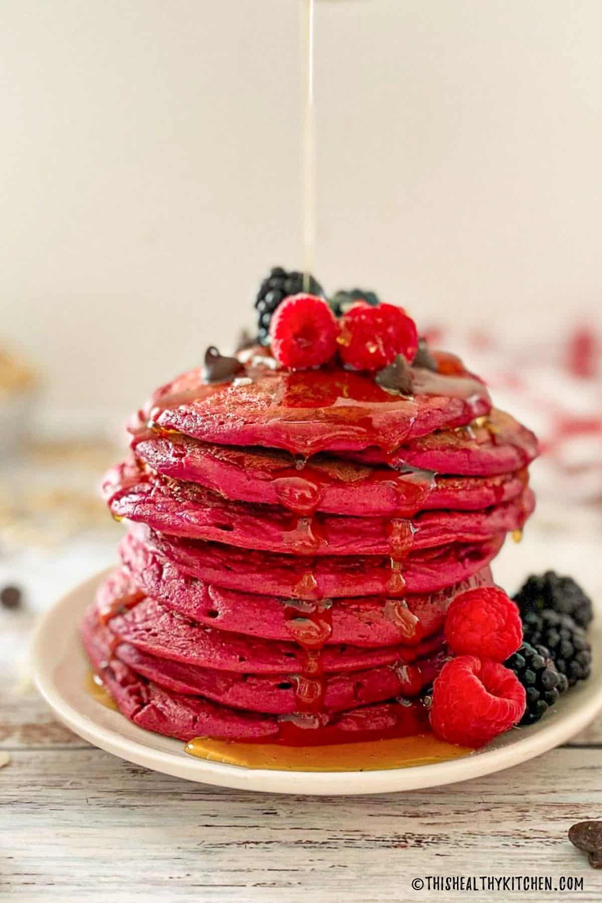 Stack of pink beet pancakes on plate with syrup dripping down the sides.