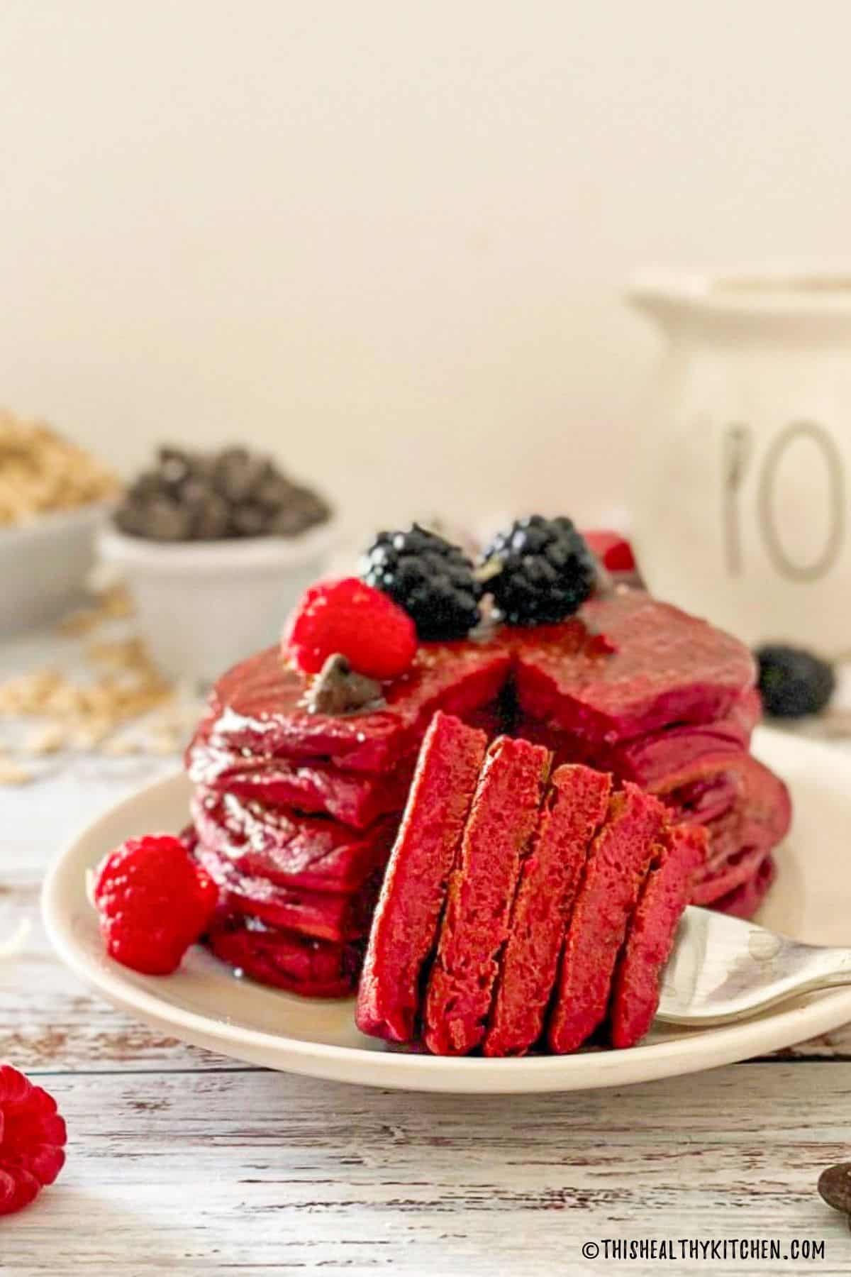 Beet pancakes stacked on plate with triangular bite cut out through the stack and on fork.