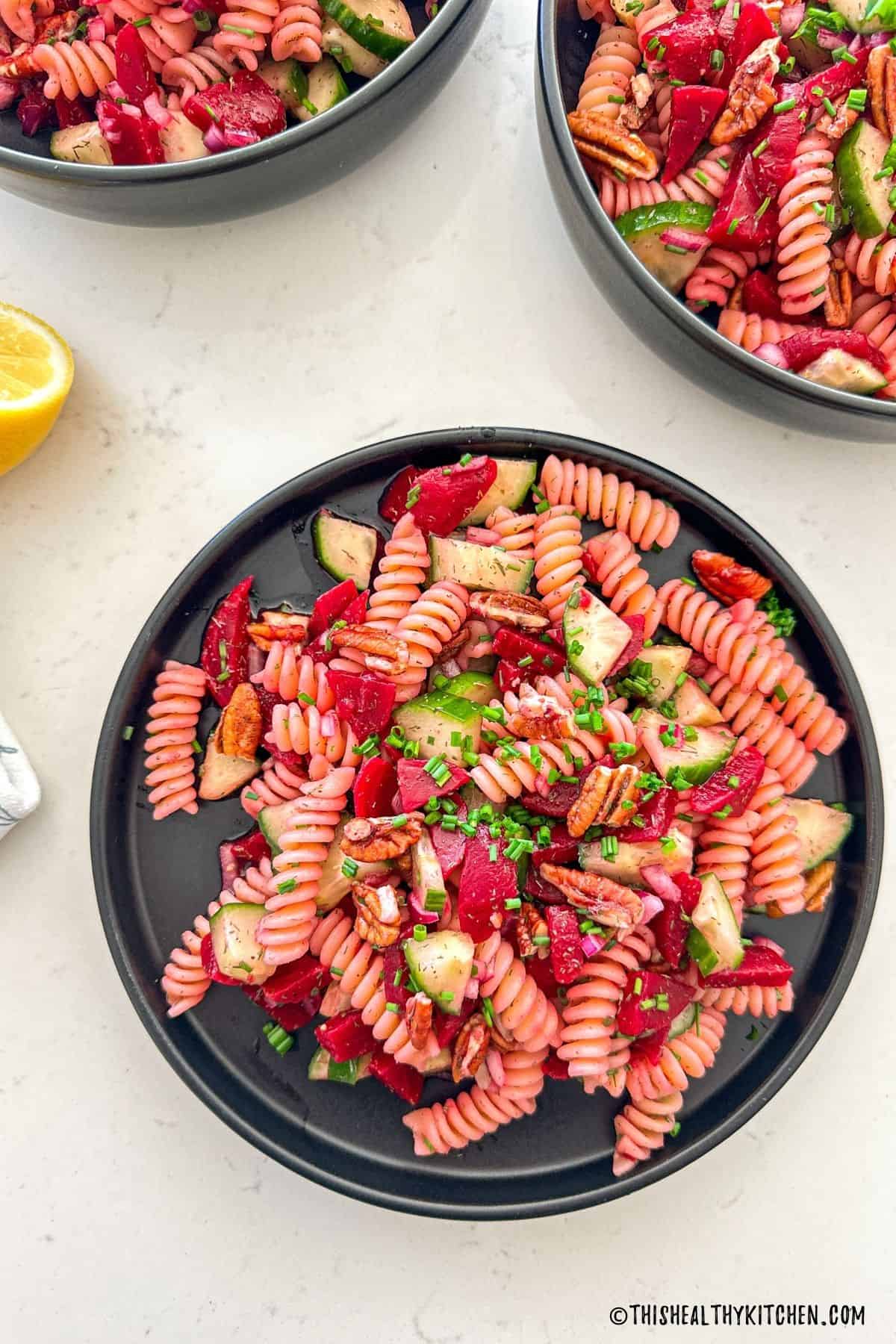 Three black plates filled with beet pasta salad.