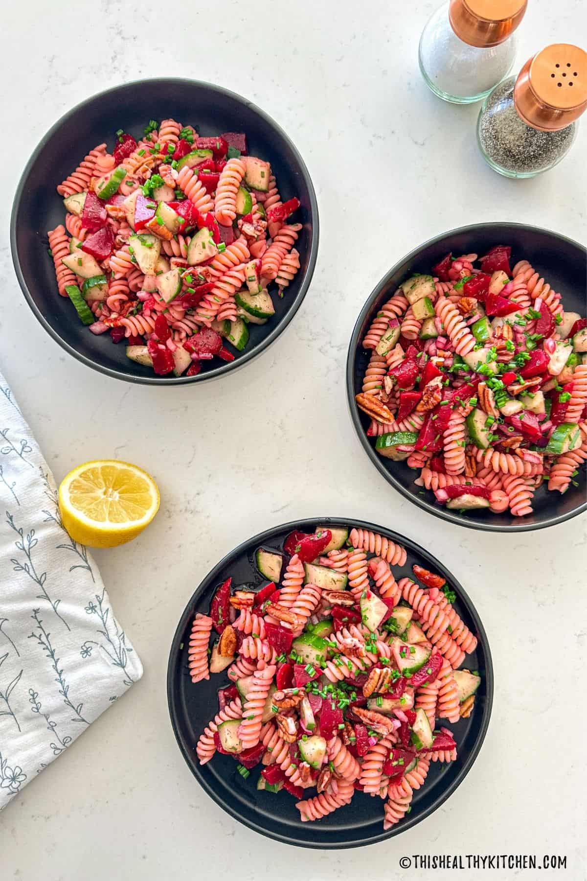 Three black plates filled with beet pasta salad.