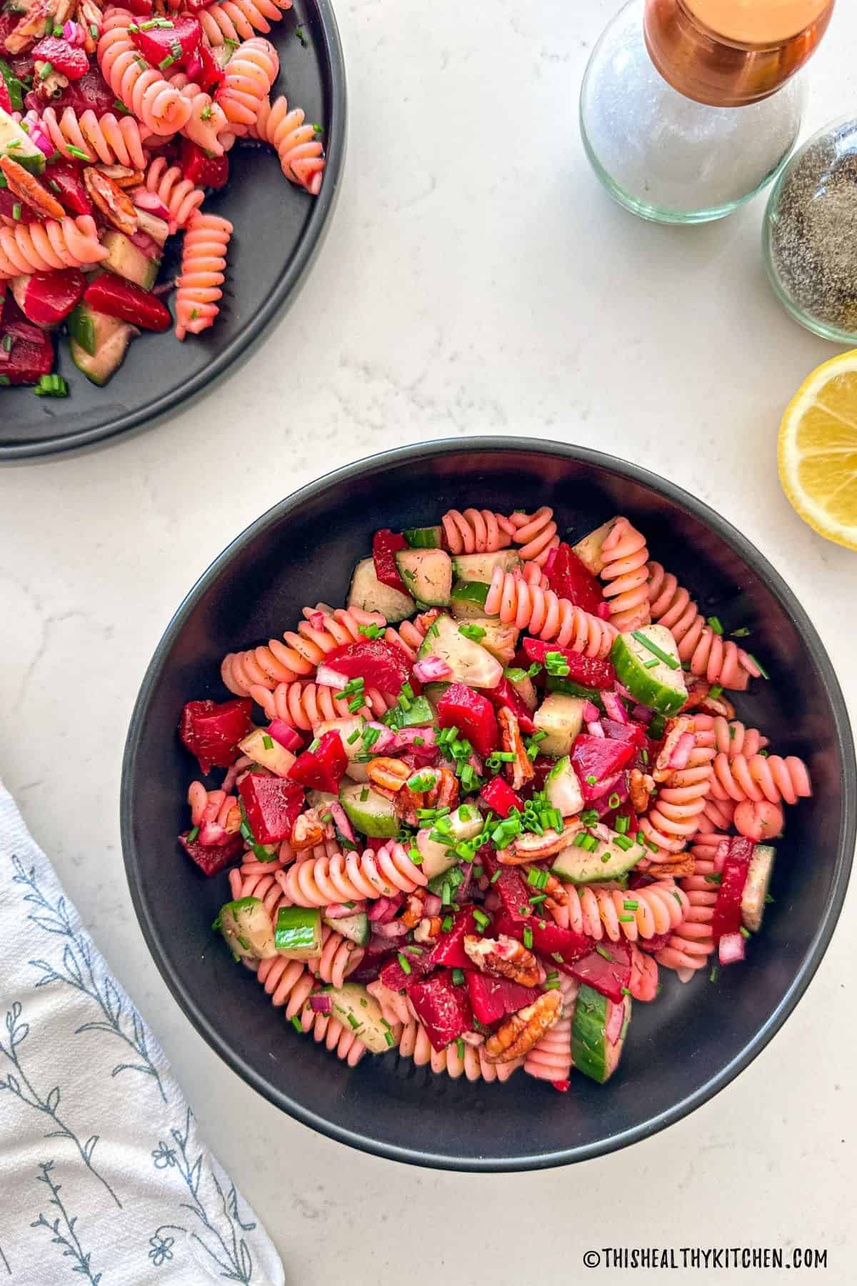 Bowl of pasta salad with beets, cucumber, chives, red onions, and pecans.