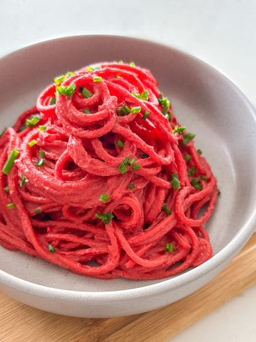 Grey bowl with spaghetti piled high with beet sauce and chives on top.
