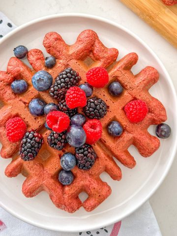 Pink beet waffle in plate with fresh berries on top.