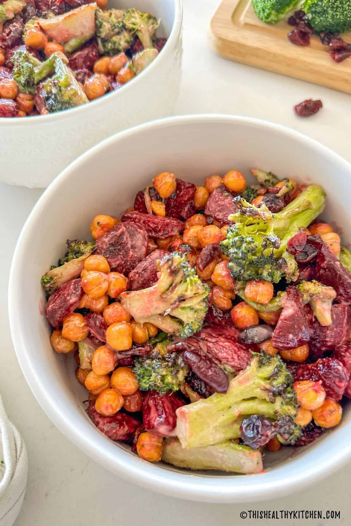 Broccoli and beetroot salad in white bowls with broccoli on cutting board in the background.