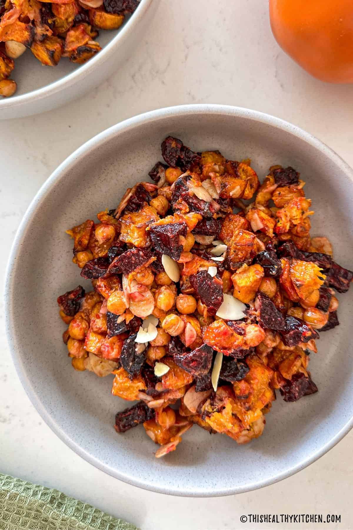 Grey bowl with beet and pumpkin salad with chickpeas, slivered almonds and cranberries.