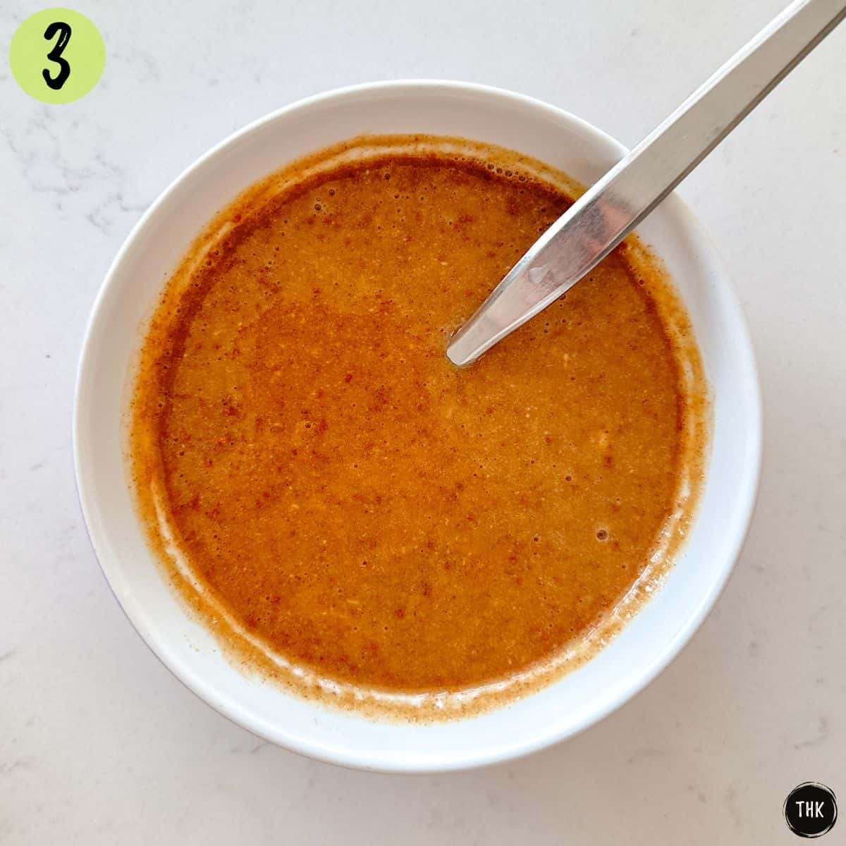 Creamy salad dressing inside small white bowl with spoon inside.