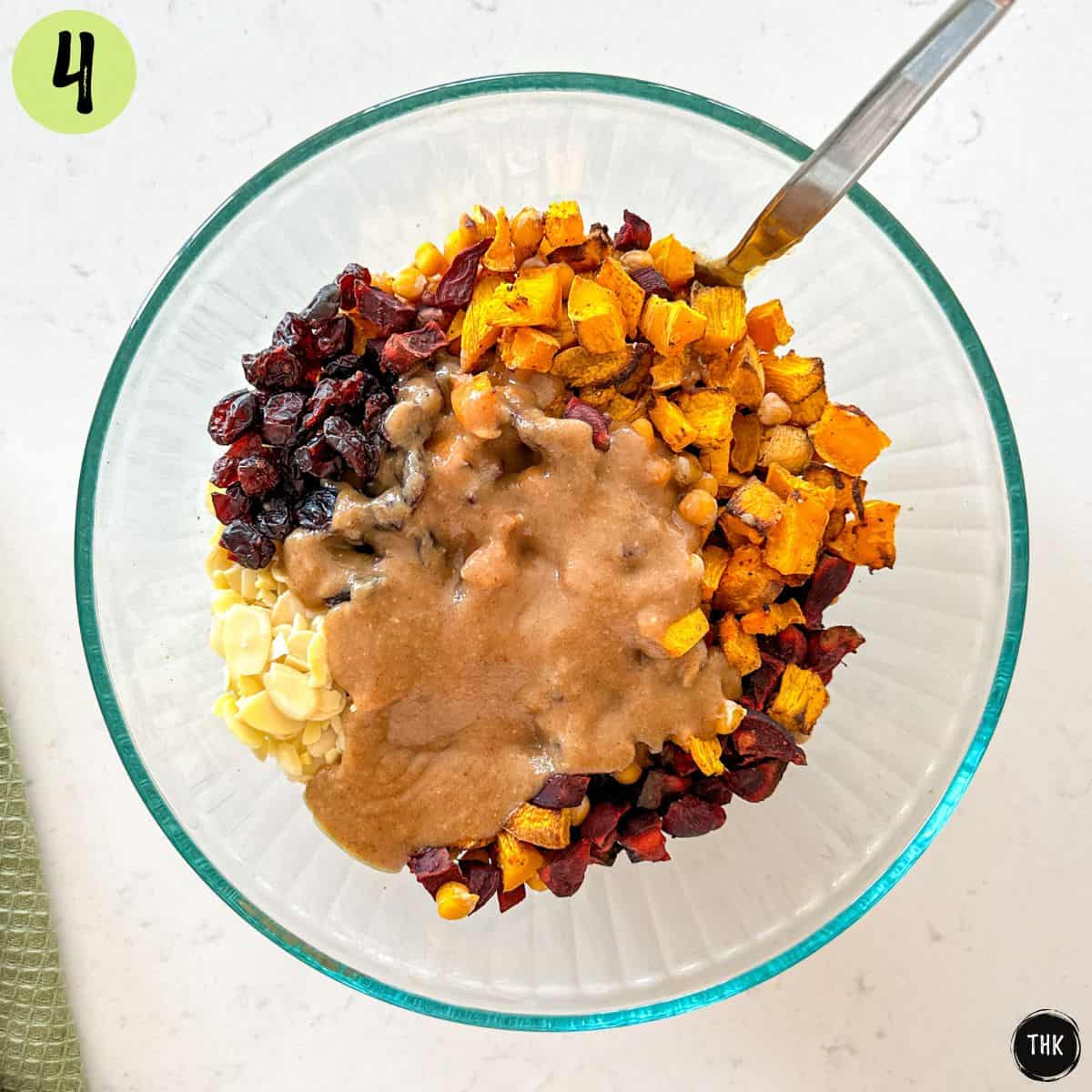 Large glass bowl with roasted beets, pumpkin, chickpeas, slivered almonds, cranberries and salad dressing on top.