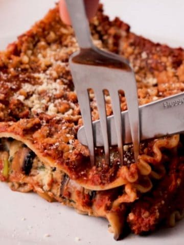 Fork and knife cutting into slice of vegan lasagna.