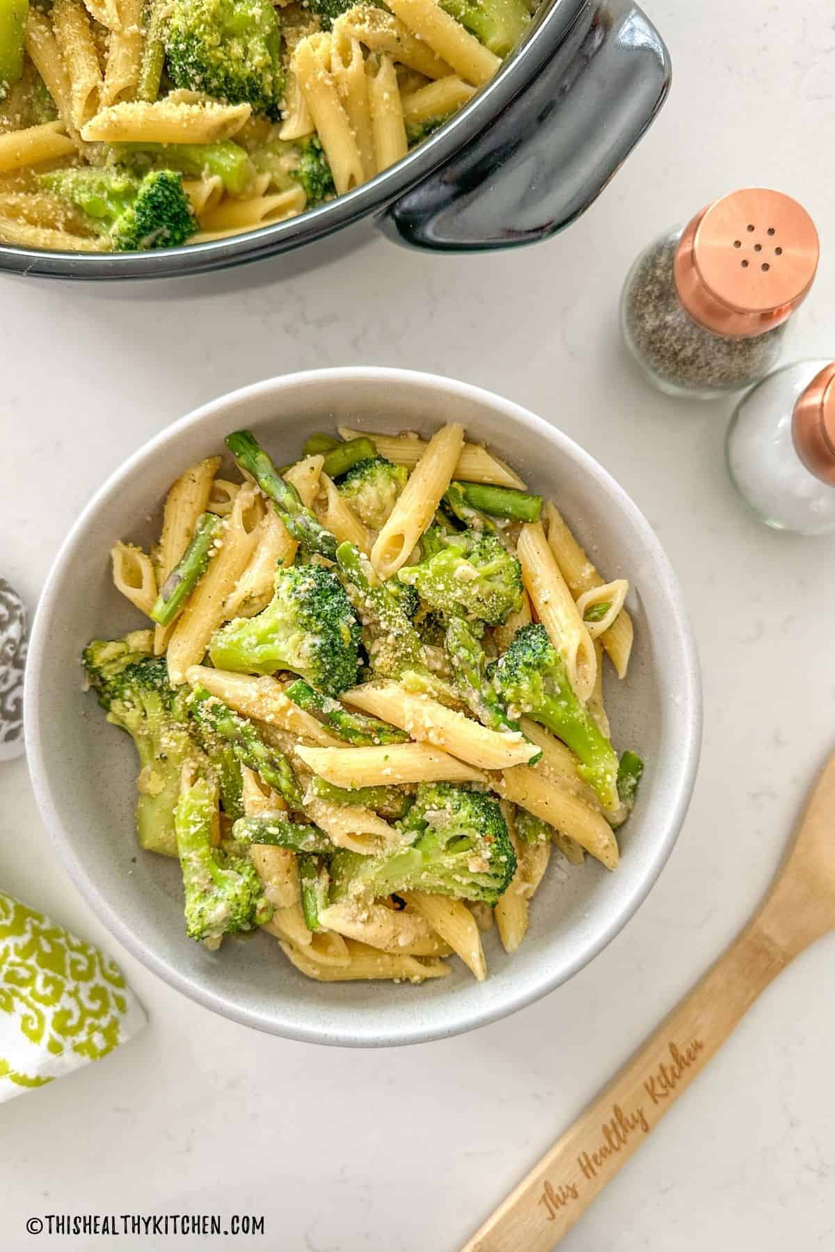 Bowl of pasta with asparagus and broccoli with more pasta in skillet beside it.