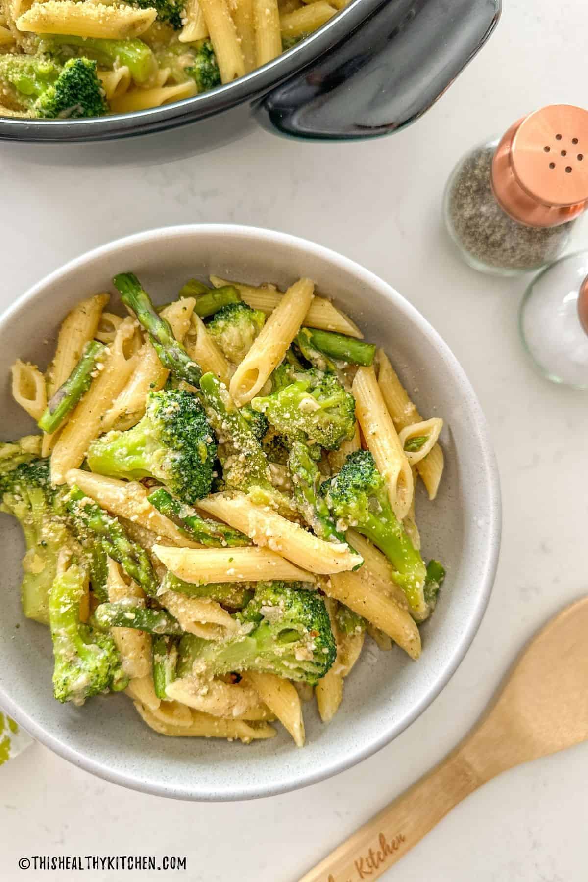 Bowl of pasta with asparagus and broccoli and vegan parmesan cheese on top.