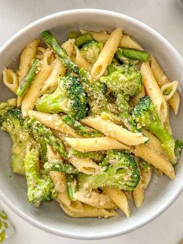 Bowl of pasta with asparagus and broccoli and vegan parmesan cheese on top.